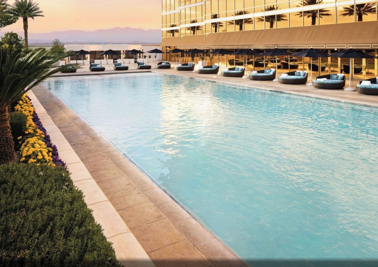 Una piscina con sillas de descanso, un edificio con amplias ventanas y vistas a la montaña.