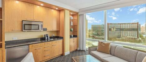 A modern kitchen with wooden cabinets, a microwave, and a coffee maker. There is a glass table and a sofa with cushions.