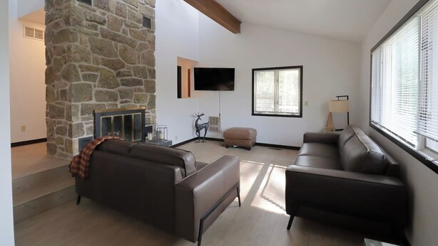 Una sala de estar con paredes de piedra, chimenea, televisor de pantalla plana y un gran ventanal.