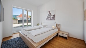 Un dormitorio moderno con un ventanal grande, una cama, una mesita de noche y una obra de arte colgada en la pared.