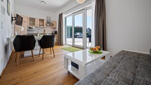 Un apartamento moderno con cocina, comedor y sala de estar. Cuenta con una puerta corrediza de vidrio al exterior, una mesa de centro blanca y un sofá gris.