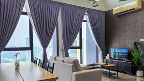 A modern living room with a sofa, dining table, and chairs, large windows with curtains, a flat-screen TV, and a potted plant. - Expressionz Suites by Manhattan Group  (Kuala Lumpur)