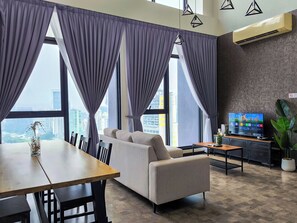 A modern living room with a sofa, dining table, and chairs, large windows with curtains, a flat-screen TV, and a potted plant. - Expressionz Suites by Manhattan Group  (Kuala Lumpur)
