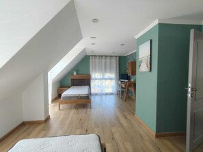 A bedroom with a sloped ceiling, a bed, a desk, and a chair.