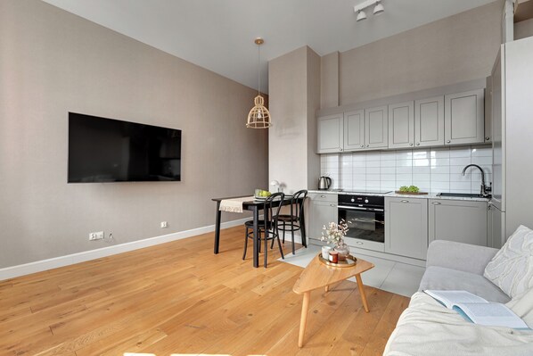 A modern kitchen with grey cabinets, a dining area with a table and chairs, and a living room with a sofa and a coffee table.