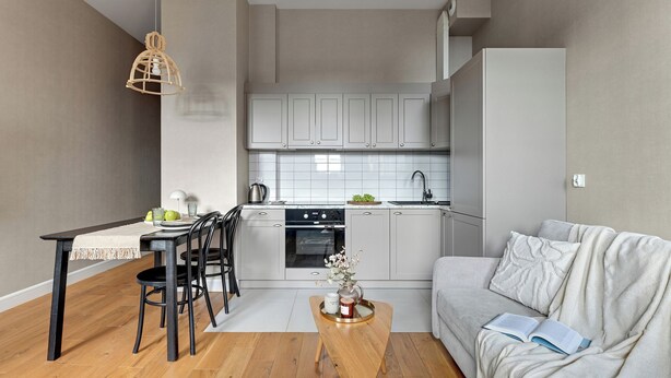 A modern kitchen with grey cabinets, a dining table with chairs, and a wooden coffee table. - Browar Hevelius Apartments by GA (Gdańsk)