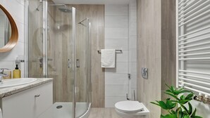 A modern bathroom with a glass-enclosed shower, a white toilet, and a marble countertop. - Browar Hevelius Apartments by GA (Gdańsk)