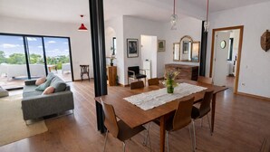 Amplia sala de estar con mesa de comedor, sofá y sillones. Un ventanal grande ofrece vistas al exterior.