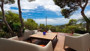 Un patio al aire libre con una mesa de madera, sillas blancas y un florero azul.