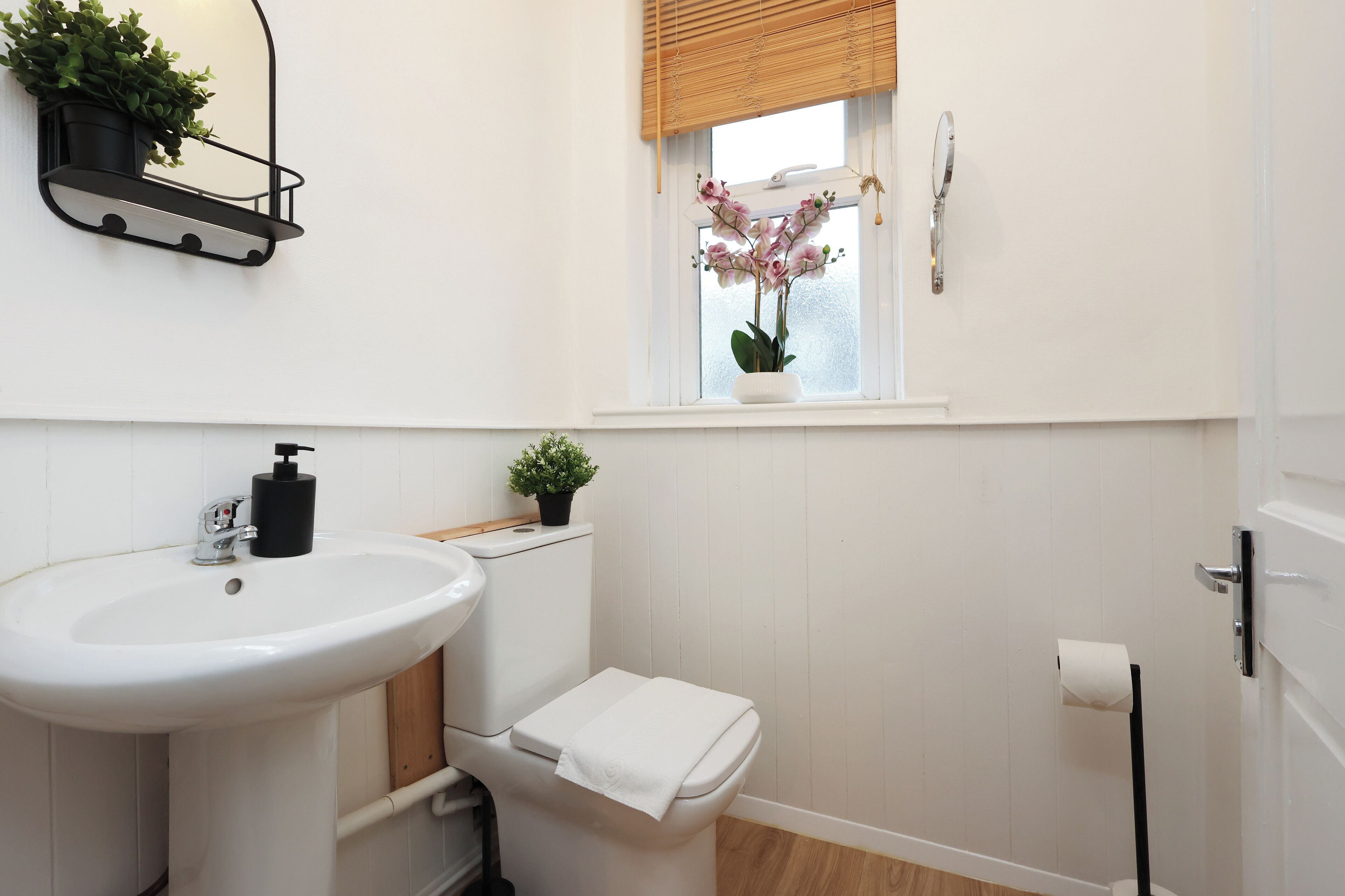 A bathroom with a white sink, toilet, and window with an orchid plant.