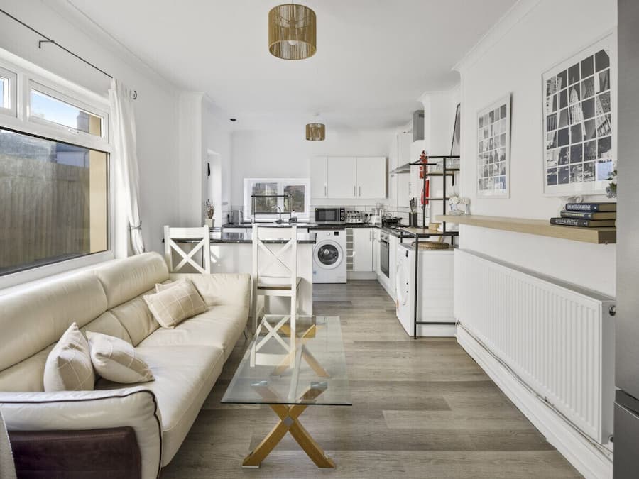 A modern kitchen with a central island, a dining area with a glass table, and a living room with a sofa.