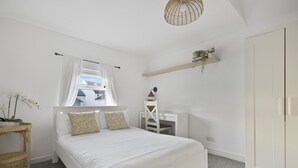 Un dormitorio con cama, escritorio, silla, armario, ventana con cortinas, y lámpara colgante.