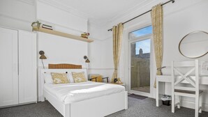A bedroom with a bed, a desk, a chair, a wardrobe, a shelf with books and a plant, and a window with curtains. - Cardiff Guesthouse & On-Street Parking (Cardiff)
