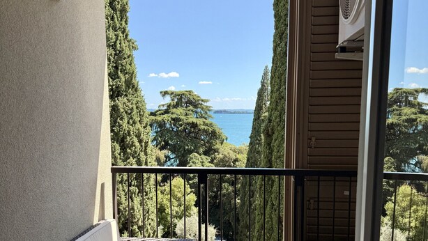 A balcony with a sofa and a table, overlooking a scenic view of trees and a body of water.