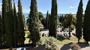 A parking area surrounded by tall cypress trees, with a view of a body of water and distant hills.