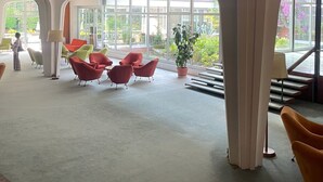 A spacious lobby with large windows, red and green chairs, and a child playing.
