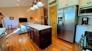 Une cuisine moderne dotée d’un îlot central, d’appareils électroménagers en acier inoxydable et d’un coin salon confortable avec une cheminée.