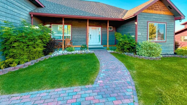 Une maison à deux étages, avec un chemin en briques menant à la porte d’entrée, entourée d’une pelouse et d’arbustes bien entretenus.