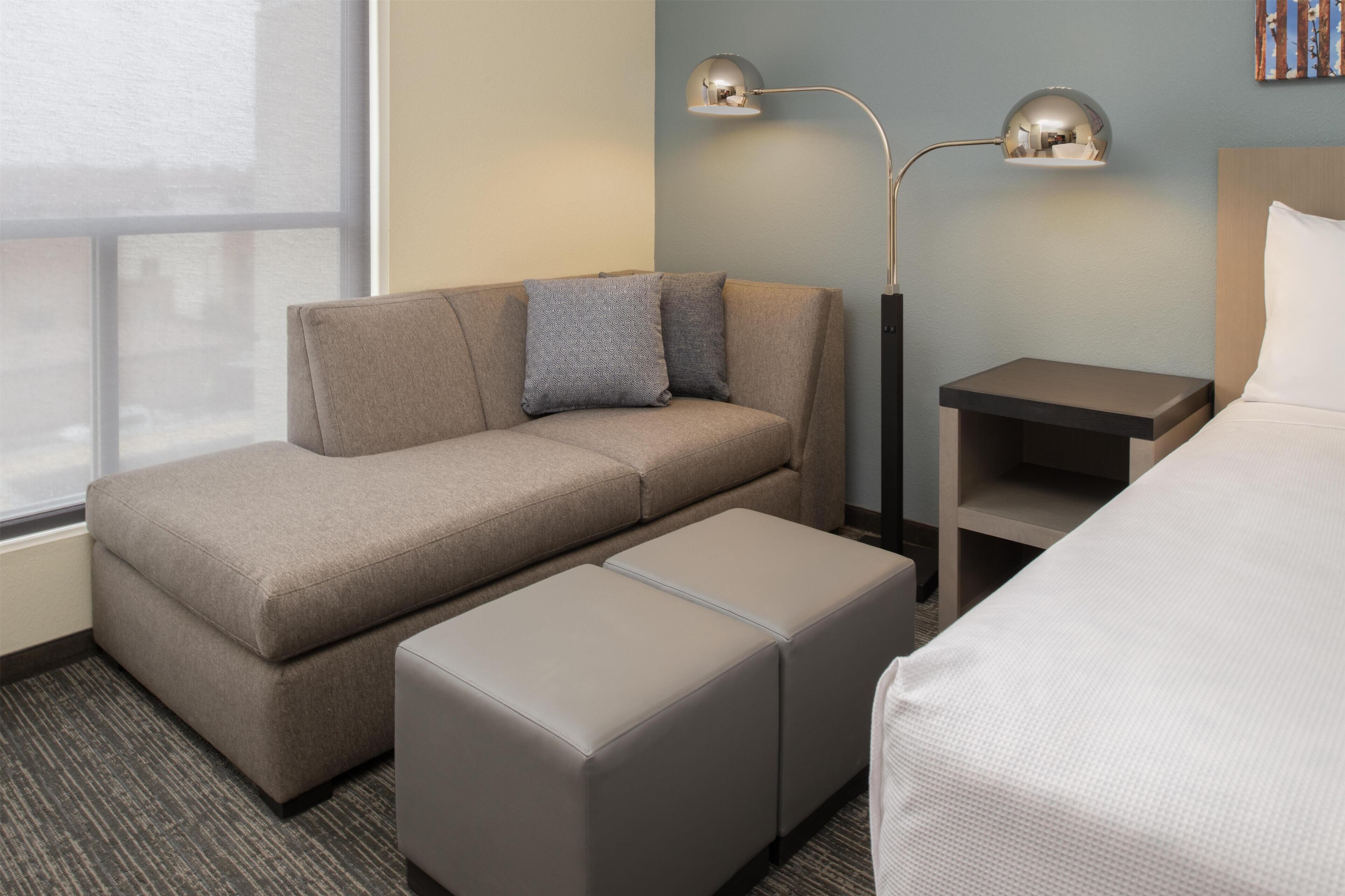 A hotel room with a sofa, ottoman, bedside tables, and a bed.