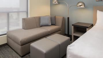 A hotel room with a sofa, ottoman, bedside tables, and a bed.