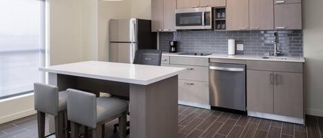 A modern kitchen with a central island, bar stools, stainless steel appliances, and a tiled backsplash.
