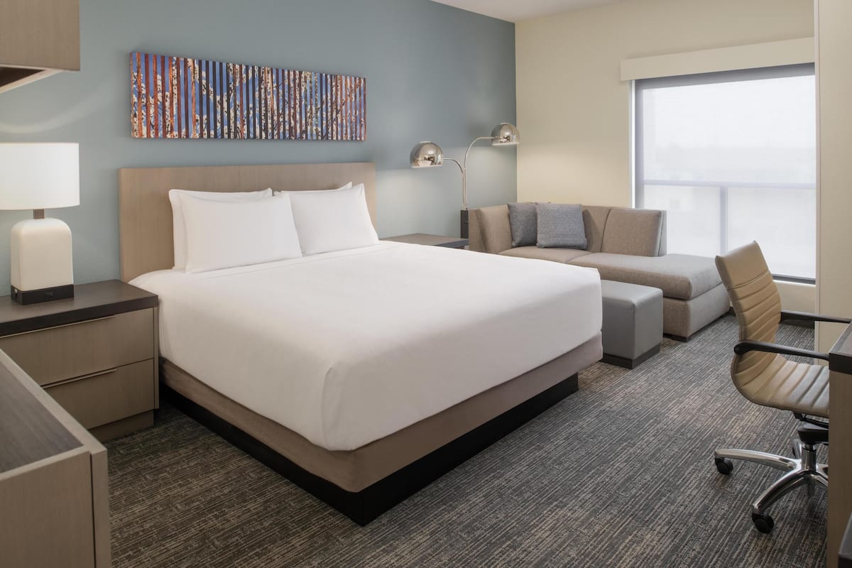 A hotel room with a large bed, a sofa, a desk, and a window.