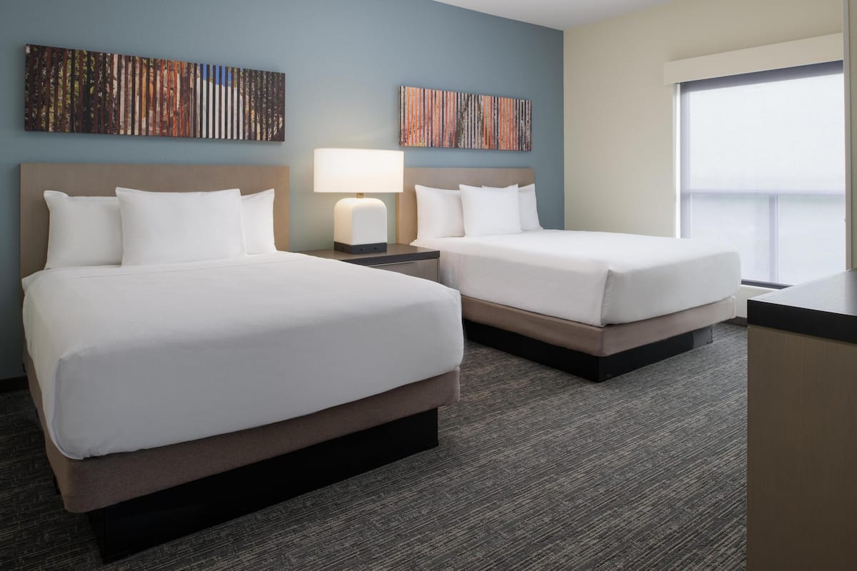 A hotel room with two beds, a nightstand with a lamp, and artwork on the walls.