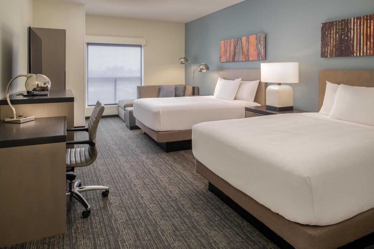 A hotel room with two beds, a desk, a chair, and a large window.