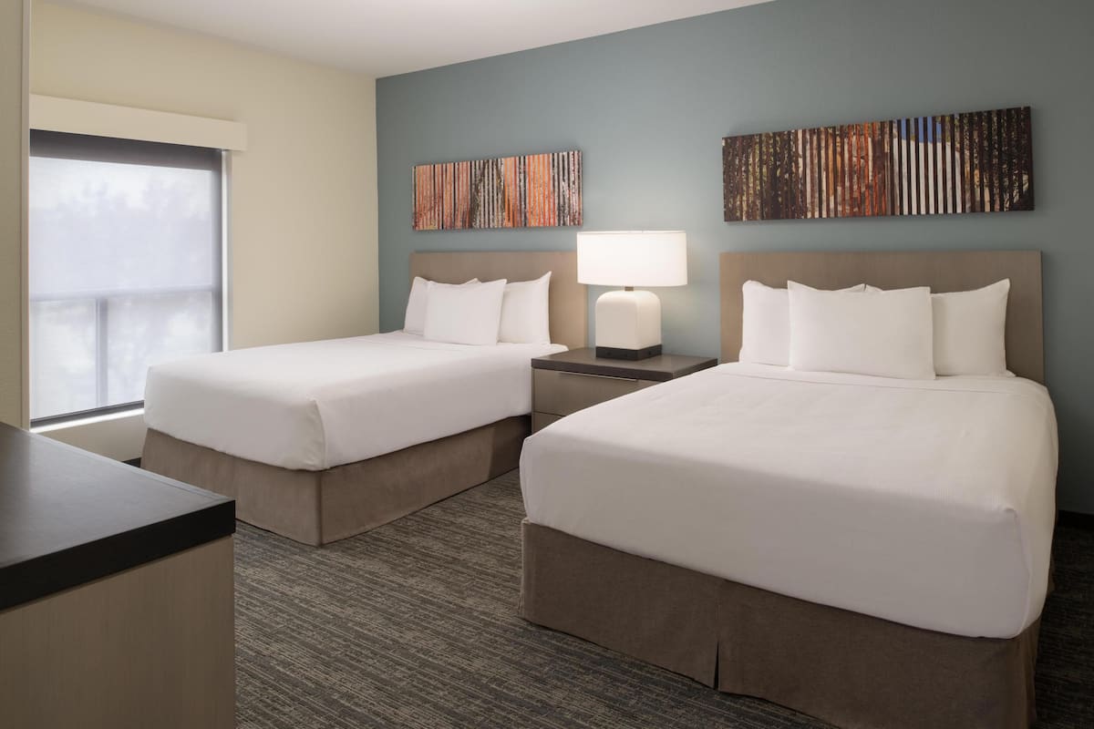 A hotel room with two beds, a desk, a lamp, and artwork on the walls.