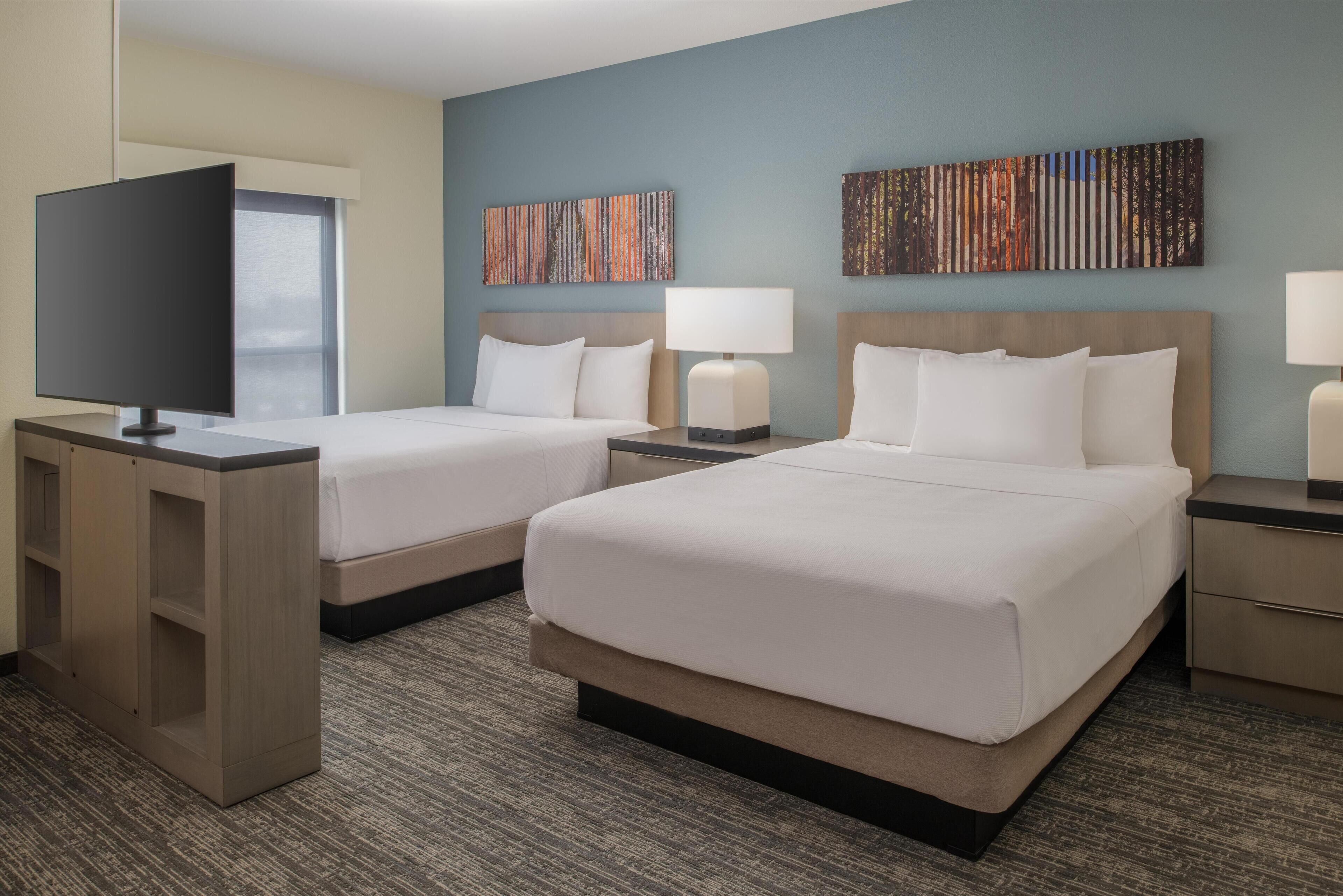 A hotel room with two beds, a TV, and artwork on the walls.