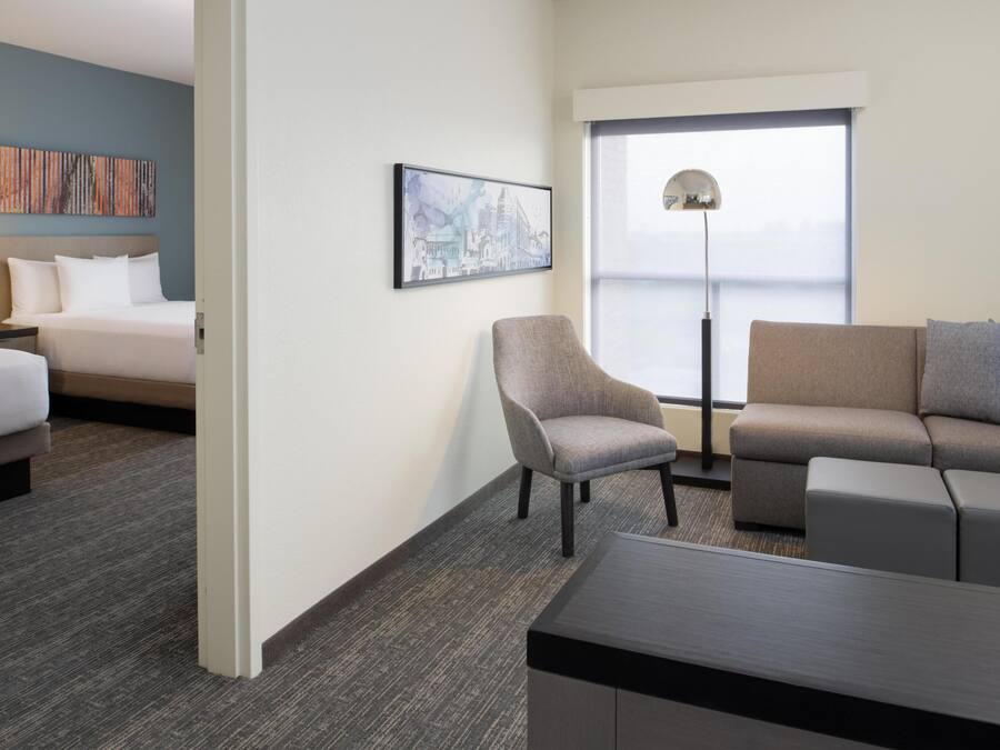 Ein Hotelzimmer mit einem Bett, einem grauen Sessel, einem grauen Sofa, einem kleinen Tisch und einem großen Fenster mit Blick.