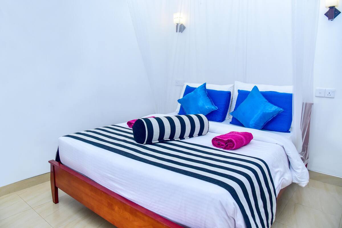 A neatly made bed with striped bedding and blue pillows, a wooden headboard, and two wall-mounted light fixtures.