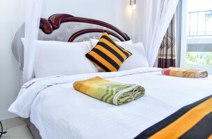 Una cama bien tendida con sábanas blancas, un cojín a rayas y una toalla enrollada.