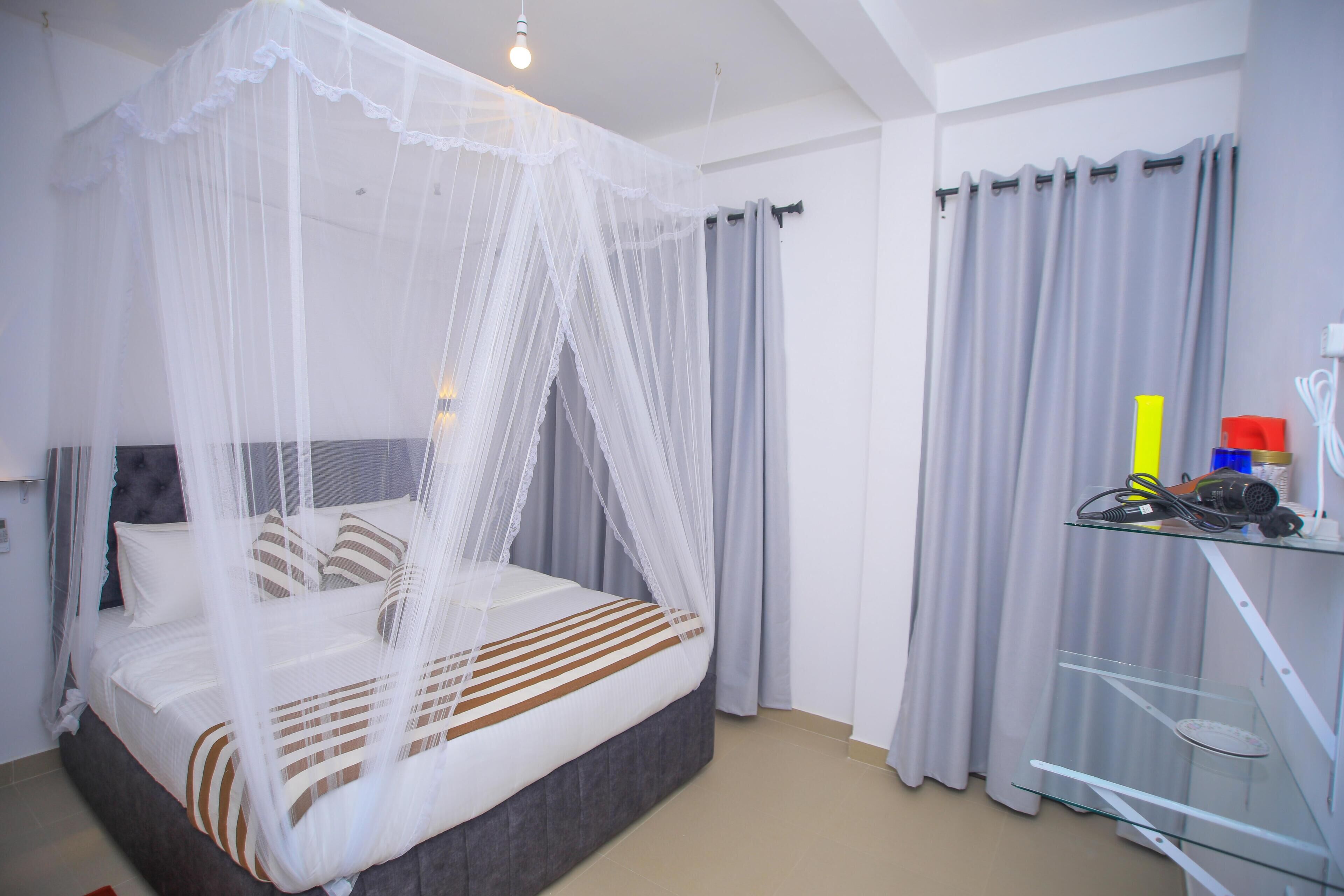 A bedroom with a bed under a white canopy, grey curtains, and a glass shelf with items.
