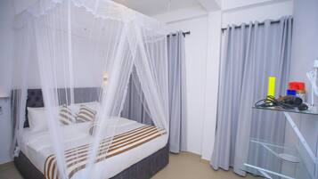 A bedroom with a bed under a white canopy, grey curtains, and a glass shelf with items.