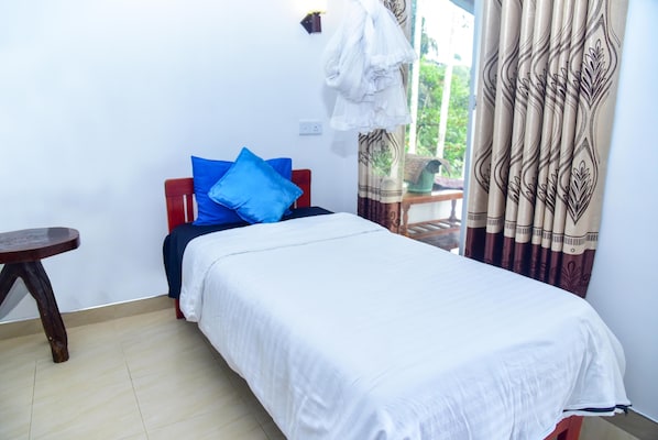 A bedroom with a bed, a small table, and a window with curtains.