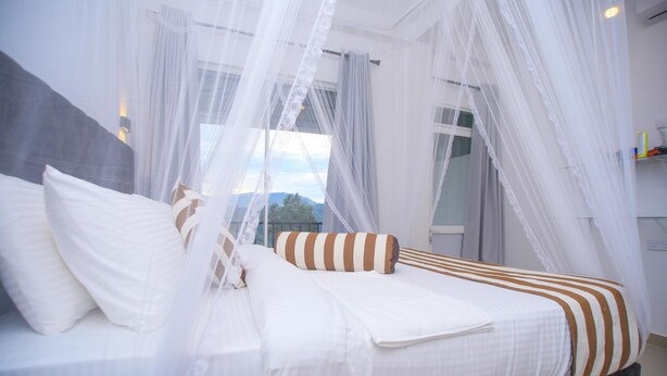 Una cama con ropa blanca y almohadas a rayas, cabecera gris y dosel.