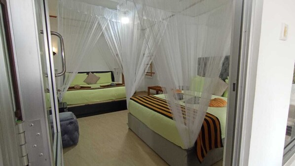 A bedroom with a bed under a mosquito net, another bed in the background, and a small table with a chair. - Ella Nimal Nest Inn (Ella)