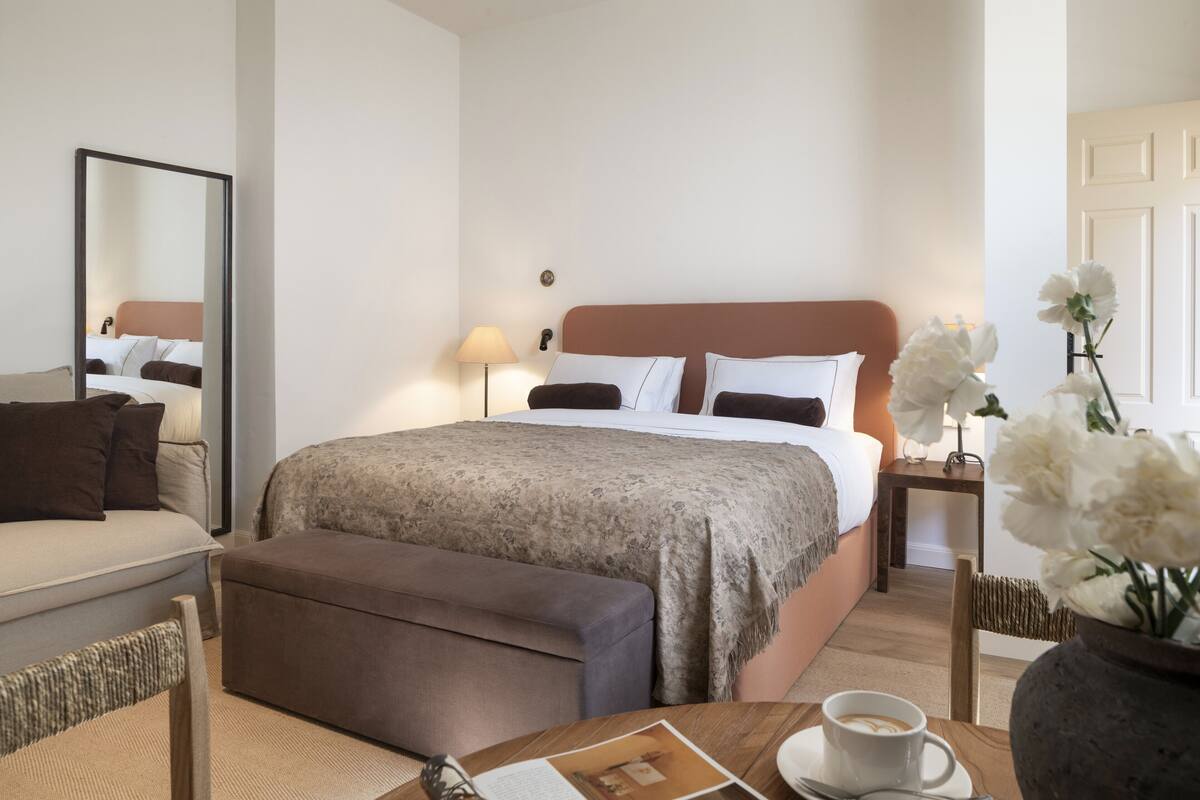 Una habitación de hotel con una cama, un sofá, una mesa de centro y un florero con flores.