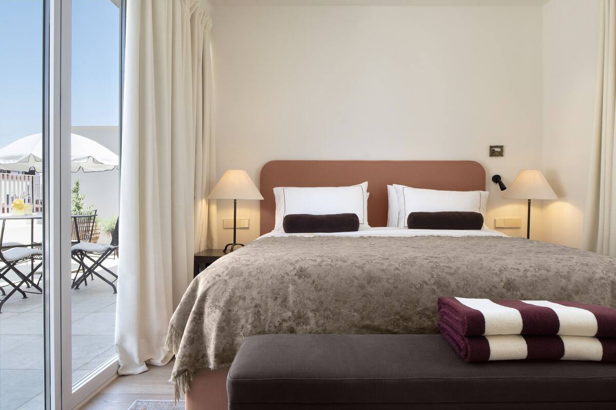 Habitación de hotel con una cama grande, dos lámparas de noche, una ventana con cortinas y vista al patio exterior.