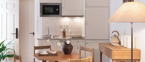 A modern kitchen with white cabinets, a microwave, a wooden dining table with chairs, a vase with flowers, and a lamp.
