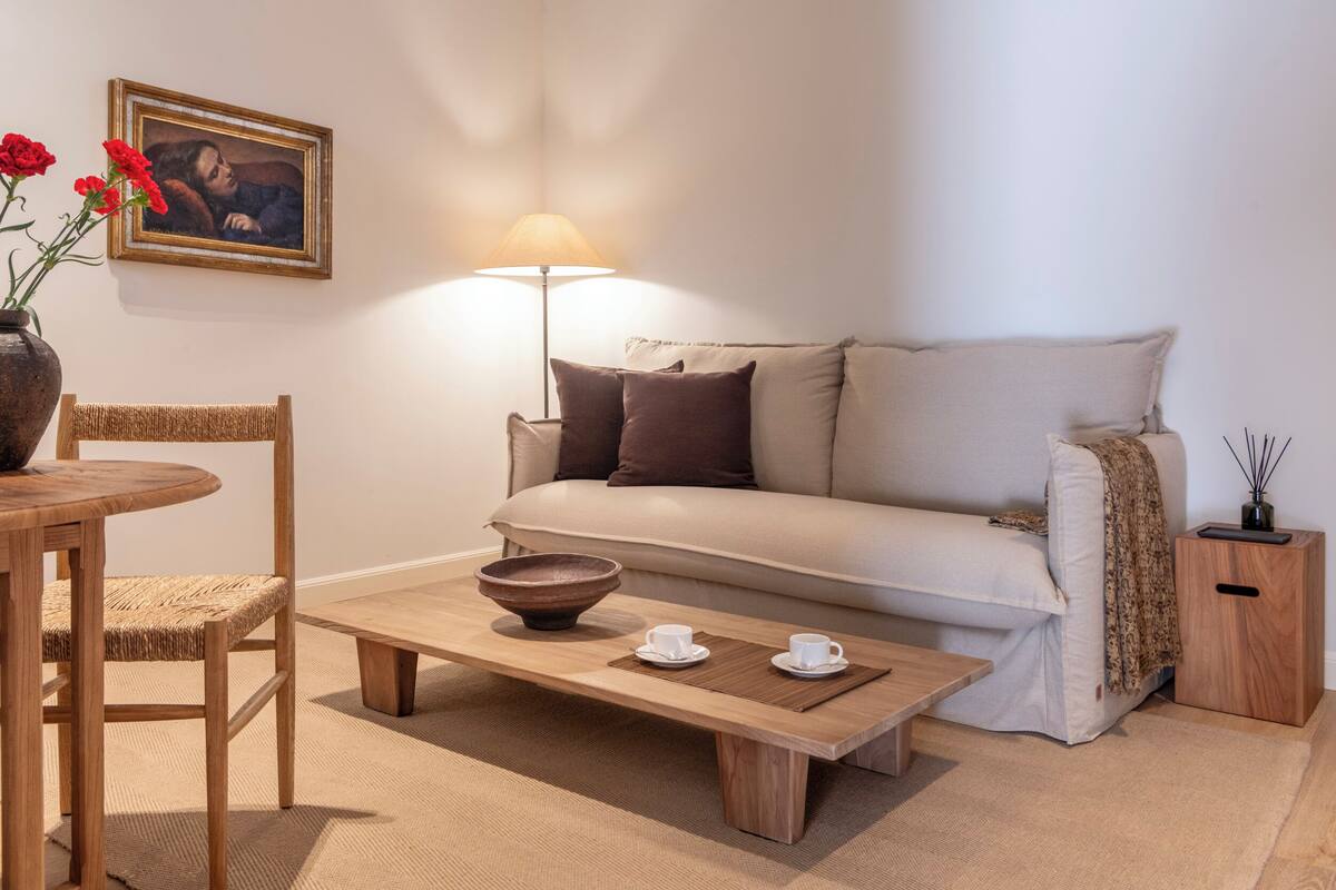 Una sala de estar acogedora con una mesa de centro de madera, un sofá color beige y una mesita auxiliar de madera, además de una lámpara.