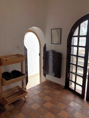 Una habitación con un banco de madera, suelo de baldosas, una puerta con ventanal y un estante fijado a la pared.