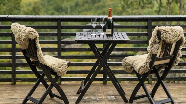 A table with a bottle and glasses on a wooden deck with two chairs, overlooking a mountainous landscape. - Stavtjørn Apline lake Haven (Vikeså)