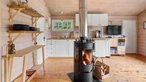 A cozy cabin interior with a wood-burning stove, wooden shelves, a kitchen area, and a window with a view of greenery. - Stavtjørn Apline lake Haven (Vikeså)