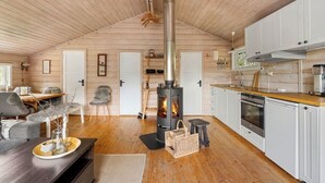 A cozy cabin interior with a central wood-burning stove, a dining area, and a kitchen with white cabinets and a wooden countertop. - Stavtjørn Apline lake Haven (Vikeså)