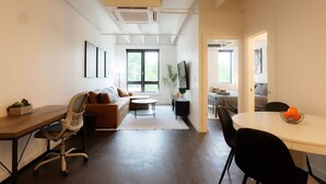 Un salon moderne comprenant un canapé, une table à manger et un téléviseur. Une fenêtre laisse entrer la lumière naturelle et offre une vue sur la verdure environnante.