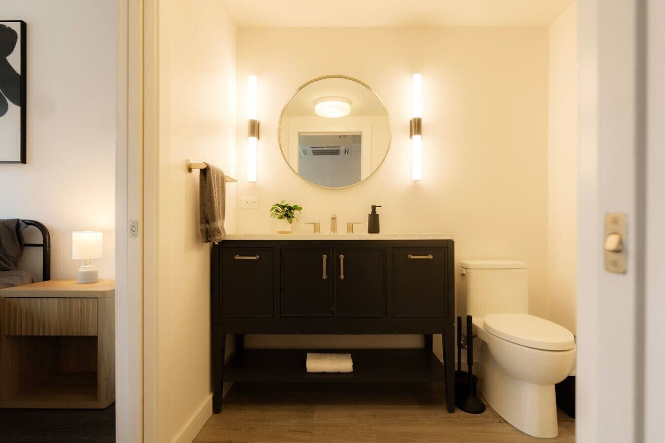 A compact bathroom with a dark wooden vanity, a round mirror, and a toilet.