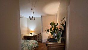 A bedroom with a bed, a desk, a chair, a dresser, a mirror, a plant, and a chandelier. - Cosy apartment (Boulogne-Billancourt)