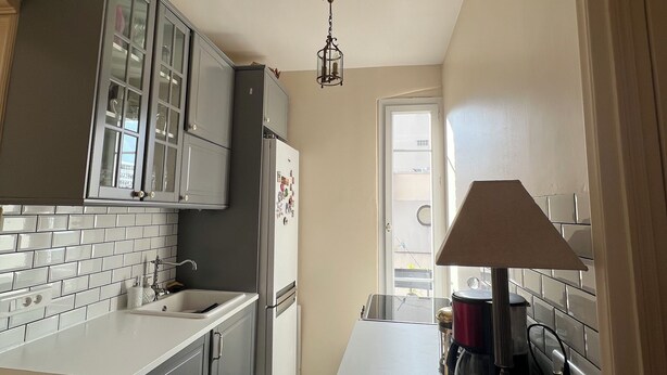 A kitchen with white tiled backsplash, grey cabinets, a white countertop, a built-in sink, a refrigerator, and a coffee maker. - Cosy apartment (Boulogne-Billancourt)